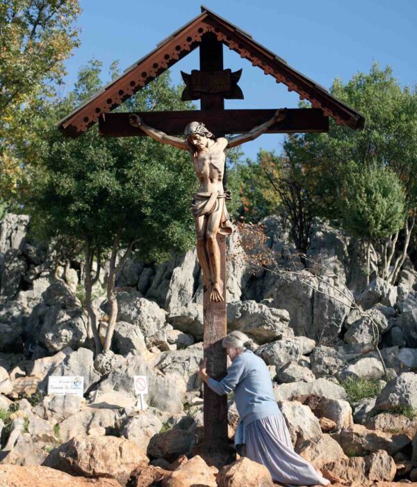 Medjugorje woman kneeling at cross on pilgrimage tour